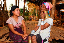 Generation gap - Kayan Lahwi woman with brass neck coils and traditional clothing chatting with her grand daughter, who is not wearing any coils and dressed in a modern style. The Long Neck Kayan (als...
