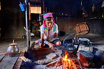 Kayan Lahwi woman with brass neck coils and traditional clothing boiling water in her house to add to her favourite drink, a liquor distilled from fermented sorghum (left in the jar).The Long Neck Kay...