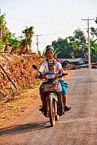 Kayan Lahwi woman with brass neck coils and traditional clothing riding a motorbike with her child. The Long Neck Kayan (also called Padaung in Burmese) are a sub-group of the Karen ethnic people from...
