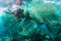 Scuba diver trying to free a large fishing net or ghost net from a coral reef, The Bahamas.
