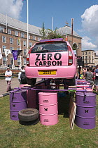 Pink car emblazoned with &#39;Zero carbon&#39;, on top of oil drums. Extinction Rebellion climate change rally. Bristol, England, UK. 16 July 2019.