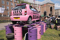 Pink car emblazoned with &#39;Zero carbon&#39; and &#39;Temperature&#39;s rising&#39;, on top of oil drums. Extinction Rebellion climate change rally. Bristol, England, UK. 16 July 2019.