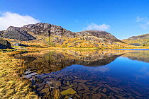 Lake Cwmorthin looking south west showing spoil heaps and ruined cottages of the disused slate mine with pieces of slate covering the bed of the lake in the foreground near Blaenau Ffestiniog, North W...