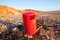 Red litter bin washed up on Rhosilli Beach, Gower, South Wales, UK, March.