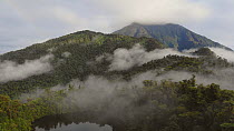Aerial timelapse rising over misty cloudforest covering the slopes of Sumaco Volcano, with a water filled crater lake in foreground, Napo Province, Ecuador, 2018. (non-ex)