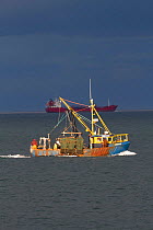 Inshore trawler in shallow coastal sea fishing area , with oil tanker in background, off County Wicklow, Republic of Ireland, June.