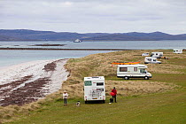 Couple with dog with numerous camper vans on East Beach, threat to nesting Little terns (Sterna albifrons). Ferry to Harris in the background, North Uist, Scotland, UK, June.