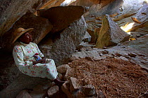 Woman sitting in cave in Anja Community Reserve. During colonial repression the local people hid in these caves, this lady was born on this &#39;nest&#39; of rice hay surrounded by stones. Granite mou...