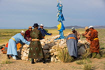 Men participating in ceremony around sacrificial altar / ovoo to worship mountain, milk libation poured as offerings to mountain deities. Great Gobi B Strictly Protected Area, Mongolia. 2018.