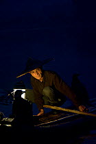 Li River fisherman in bamboo hat on raft with cormorants trained to bring back fish. In early morning, Yangshuo, Guangxi, China. 2009.
