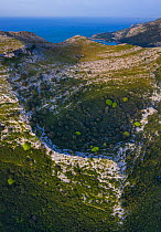 Dolina depression in limestone cliff, Mediterranean forest with Holm oak (Quercus ilex) forest on slopes. Cantabrian sea in background, aerial view. Liendo Valley, Montana Oriental Costera, Cantabria,...