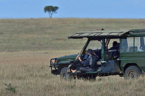 Camerawoman waiting in vehicle, looking out over the savanna, Masai Mara, Kenya. March.