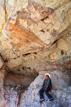 Guide sitting beneath prehistoric rock painting. El Palmarito cave, Santa Martha Sierra, El Vizcaino Biosphere Reserve, Baja California Peninsula, Mexico. 2008.