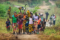 Women and children walking along road carrying fire wood and waving, Democratic Republic of Congo. May 2017.
