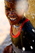Child cooling down under water falling from artificial well used by nomads and shepherds to provide water to sheep and dromedaries. Sahara Desert, Africa.