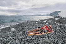 Tim Flannery in summer clothing, reading his best-selling book &#39;The Weather Makers&#39; on an icy pebble beach, Robert Point, Antarctic Peninsula, Antarctica, to illustrate the warming of the Anta...