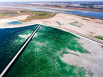 Service road crossing an abandoned pond used for the disposal and stacking of phosphogypsum with crystallised patterns and shallow, but highly toxic radioactive green water in Huelva, Southern Spain....
