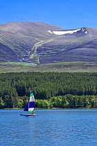 Sailing boat on Loch Morlich in front of the Cairngorm Mountains, Cairngorms National Park, Badenoch and Strathspey, Highland, Scotland, UK. June 2018