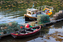 Moored small fishing boat and lobster pots / prawn creels stacked on jetty in the Plockton Harbour, Scottish Highlands, Scotland, UK