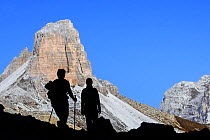 Two mountain walkers silhouetted against Torre dei Scarperi / Schwabenalpenkopf, Sexten Dolomites, Parco Naturale Tre Cime, South Tyrol, Italy, October 2019