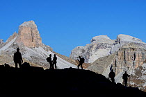 Mountain walkers silhouetted against Torre dei Scarperi / Schwabenalpenkopf, Sexten Dolomites, Parco Naturale Tre Cime, South Tyrol, Italy, October 2019