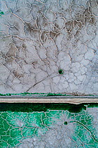 Service road crossing an abandoned pond used for the disposal and stacking of phosphogypsum with crystallised patterns and shallow, but highly toxic radioactive green water in Huelva, Southern Spain....