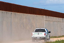Border patrol driving on no-man&#39;s land side of 30 foot concrete and steel border wall. On private farm, Mission, Hidalgo County, Texas, USA. 2019.
