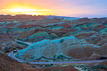 Tourist bus on winding road through Rainbow Mountains, eroded hills of sedimentary conglomerate and sandstone. At sunrise, Zhangye National Geopark, China Danxia UNESCO World Heritage Site, Gansu Prov...
