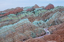 Tourist bus on winding road through eroded hills of sedimentary conglomerate and sandstone. Rainbow Mountains, Zhangye National Geopark, China Danxia UNESCO World Heritage Site, Gansu Province, China....