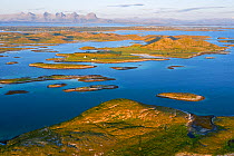 Aerial view of sporadically inhabited islands, islets and skerries, illuminated by the warm evening light. Landmark mountain the Seven Sisters can be seen in the background. Oksningan, Heroy, Helgelan...
