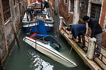 Local men recovering small capsized boat during flooding in Venice, Italy, December 2019.