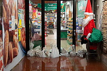 Shop with sandbags during flooding in Venice, with Father Christmas decoration, Italy, December 2019.