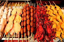 Butterfly pupae on skewers, next to chicken and crab skewers. Open-air food market in central Beijing, China.