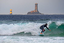 Lighthouse La Vieille and surfer in wetsuit riding a wave on surfboard at the Pointe du Raz, Finistre, Brittany, France, September 2019