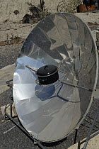 Solar cooker, with a reflective parabolic dish focusing heat from the sun onto a metal casserole pot, within a renewable energy display at ITER Bioclimatic village, near El Medano, Tenerife, August.
