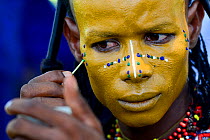 Man from Wodaabe nomadic tribe painting face for Gerewol celebration, a gathering of different clans in which women choose a husband. Men dress in best clothes and ornaments and sing and parade in fro...