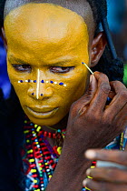 Man from Wodaabe ethnic group painting face for Gerewol celebration, a gathering of different clans in which women choose a husband. Men dress in best clothes and ornaments and sing and parade in fron...
