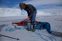Scientist preparing ice fishing gear next to a tide crack, Dumont d&#39;Urville station, Antarctica. December 2016.