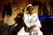 Voodoo healer / azeto of Djenan Temple, motorbike and mural of lion in background. Abomey, Benin, 2020.