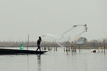 Tofinou fisherman casting net from boat on in Lake Nokoue, Oueme River delta. Ganvie, known as African Venice, Benin, 2020.