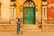 Woman carrying shopping on head past the Great Mosque,Porto Novo, Benin, 2020.