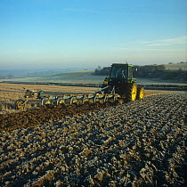 Tractor with a non-reversible, 7 coulter Ransome plough, ploughing stubble through the frost on a cold autumn morning, Hampshire, England, UK. November,