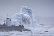 Waves crashing against coast at Porthcawl Lighthouse during Storm Ciara, people storm watching on sea wall. Mid Glamorgan, Wales, UK. February 2020.