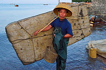 Fisherman of Shi Ma Jiao harbour carrying raft made of styrofoam blocks which he uses to reach his fishing boat at high tide, Guangdong province, China November 2015.