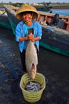 Sea bass and happy fisherwoman holding it, Shi Ma Jiao harbour, Guangdong province, China November 2015.