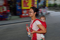 Woman out shopping with baby on back, Mother and baby out shopping and walking in the street, Old Julong village, Guangzhou, Guangdong, China November 2015.