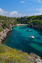 Yachts moored in the cove at Cala Pi, viewed from narrow cliff top coast path, Mallorca south coast, August 2018.