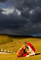 Buddhist novices studying and reciting mantra, outdoors in steppe under stormy sky. Ganden Thubchen Choekhorling Monastery, Litang, Garze Tibetan Autonomous Prefecture, Sichuan, China. October 2016.