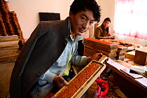 Craftsman in workshop with wooden plate for printing Buddhist prayers. Palpung Monastery, Kham, Dege County, Garze Tibetan Autonomous Prefecture, Sichuan, China. 2016.