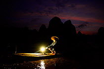 Traditional Chinese fisherman on raft on Li River at dusk, Karst peaks silhouetted in background. Yangshuo, Guangxi, China. 2016. Editorial use only.